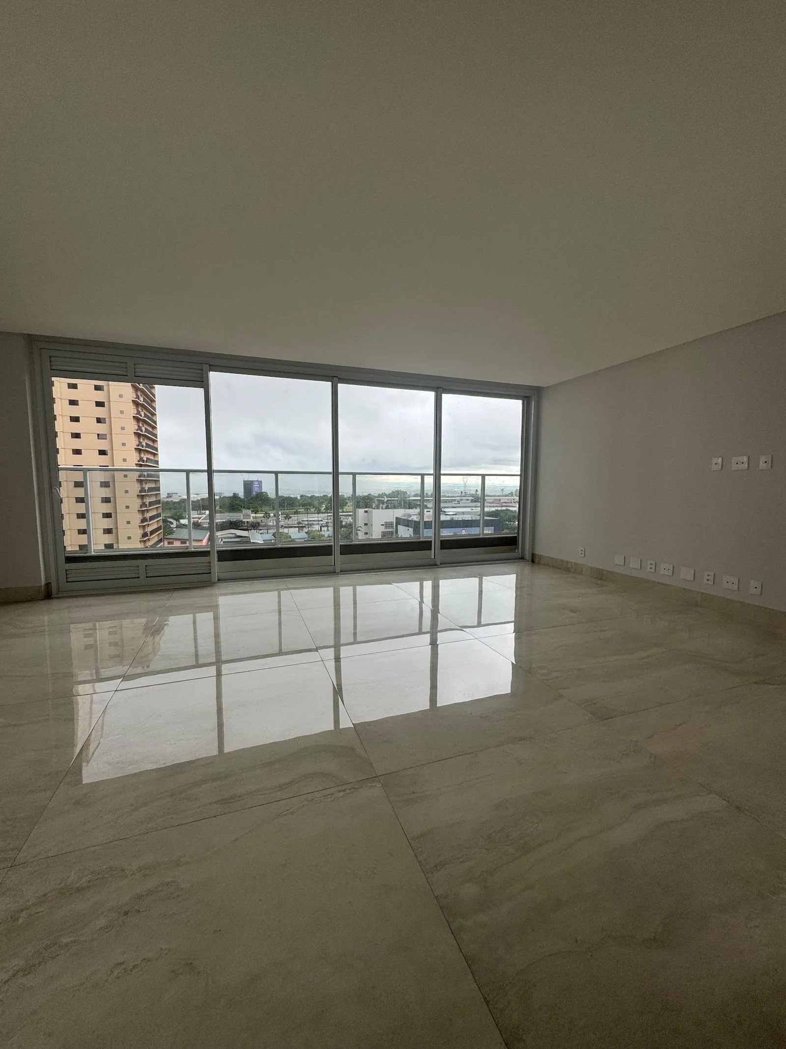 Living vazio da unidade 1001, com esquadria de vidro do piso ao teto e piso de porcelanato polido